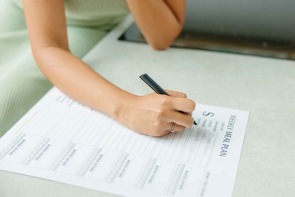 Person writing a meal plan, How to Avoid Weight Gain Over Thanksgiving